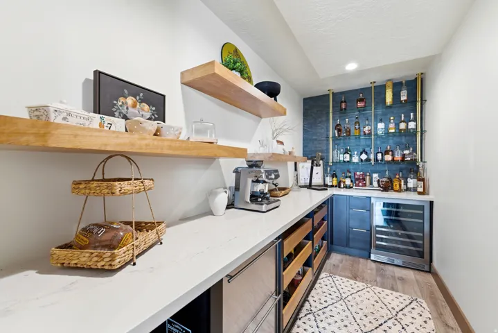 Custom beverage station featuring a built-in wine refrigerator, brass-finished shelving, and a textured blue accent wall