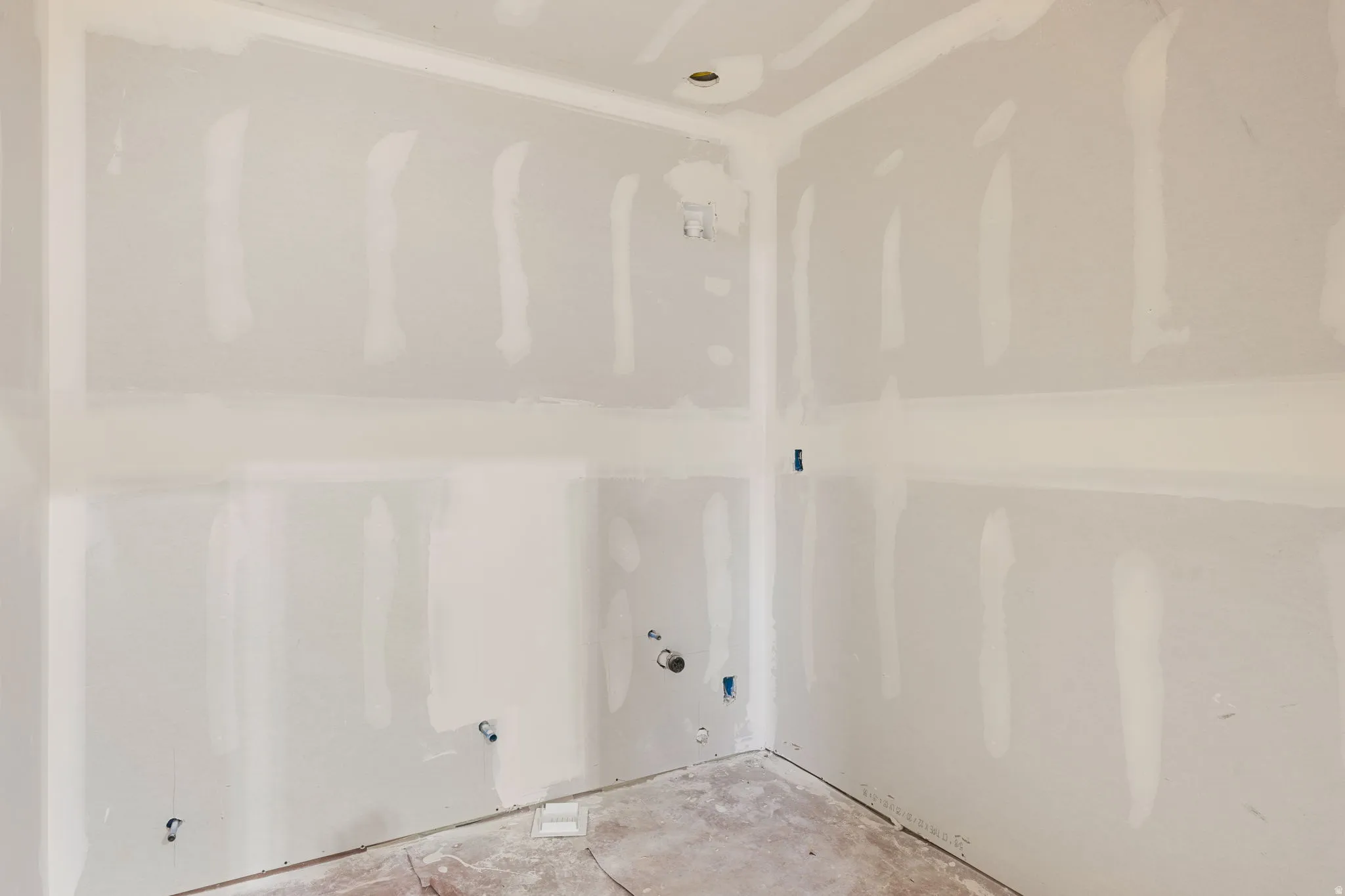 Unfinished interior space with drywall installation, exposed utility connections, and a concrete subfloor