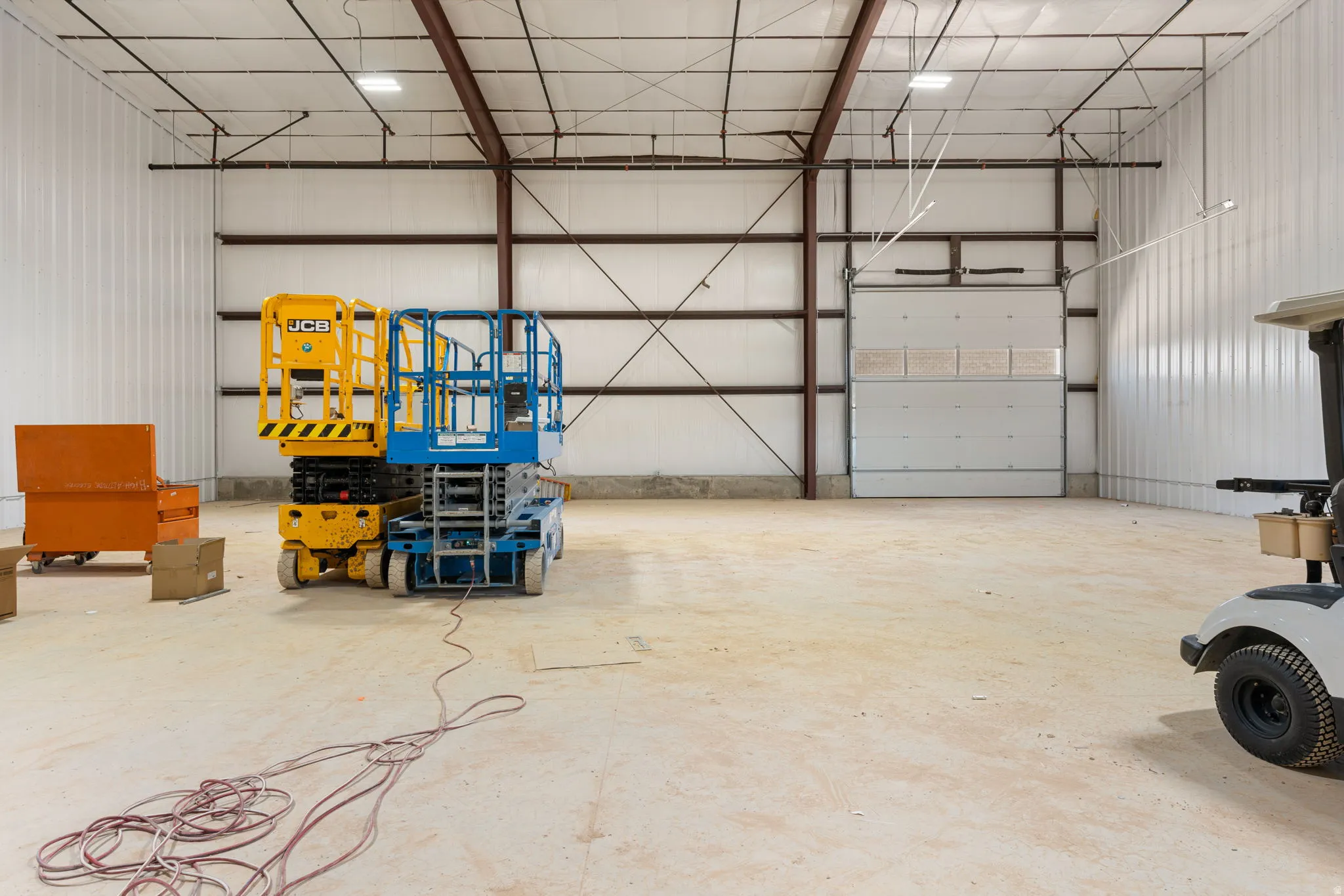 Spacious warehouse interior featuring a concrete floor, high ceilings with exposed metal beams, white corrugated metal walls, and a large roll-up door
