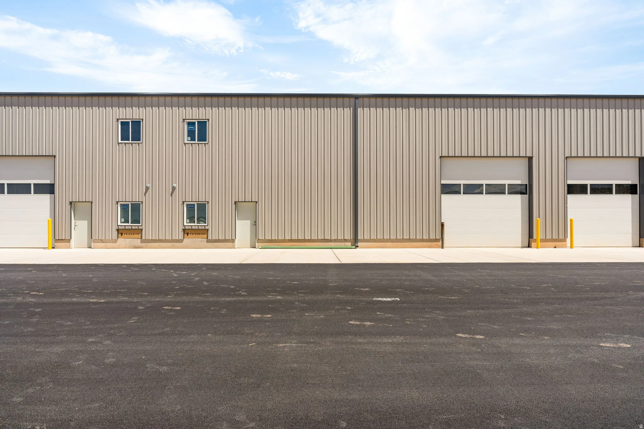 Industrial building with corrugated metal siding, multiple roll-up garage doors, and a paved asphalt lot