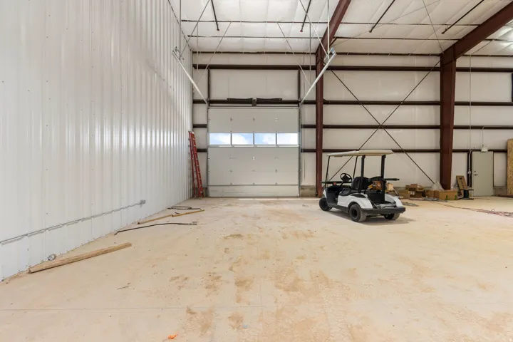 Spacious interior featuring a large overhead door with window panels, high ceilings with exposed structural beams, and concrete flooring