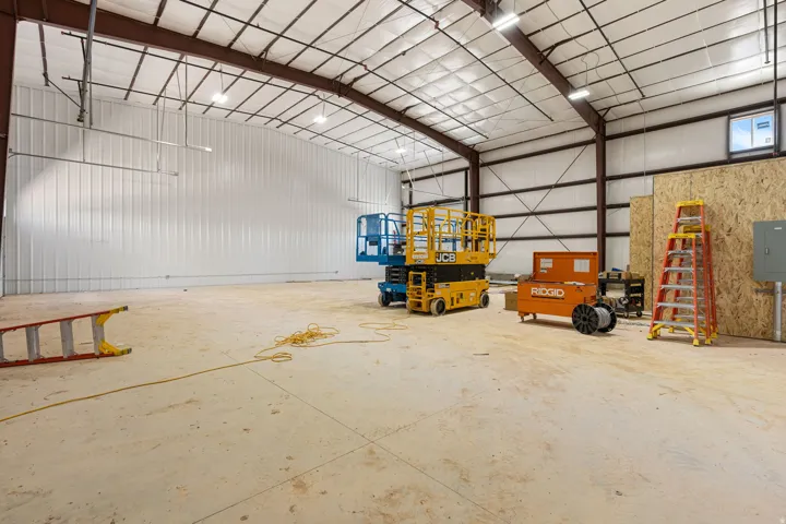 Spacious commercial interior featuring a high ceiling, exposed steel structural beams, abundant overhead lighting, and concrete flooring