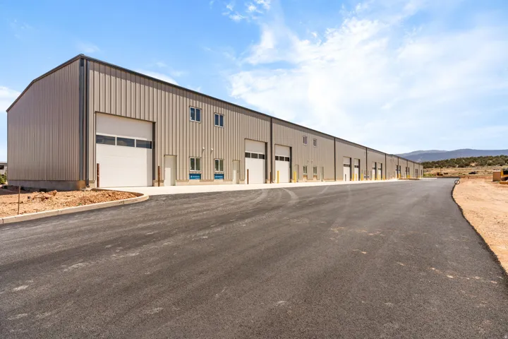 Expansive light tan corrugated metal industrial building featuring multiple roll-up garage doors, ground-level entry doors, and upper-level windows