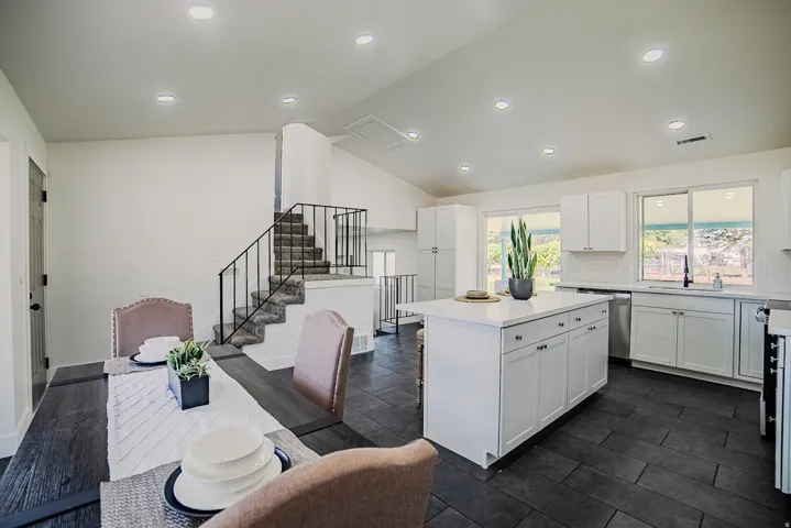 Open-concept living area featuring a modern kitchen with white cabinetry, a center island with a light-toned countertop, and dark-toned tile flooring