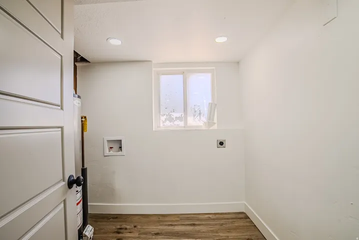 Dedicated utility space featuring wood-finish flooring, a modern white paneled door, recessed ceiling lighting, and a window for natural illumination