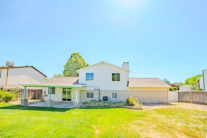 Rear exterior featuring a covered patio, sliding glass door, and a large grassy area