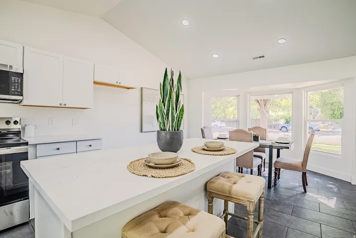 Modern kitchen featuring a large island with a white countertop, white cabinetry, stainless steel appliances, and dark tile flooring
