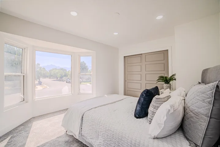 Spacious bedroom featuring a bay window, plush carpet flooring, recessed lighting, and a closet with paneled sliding doors