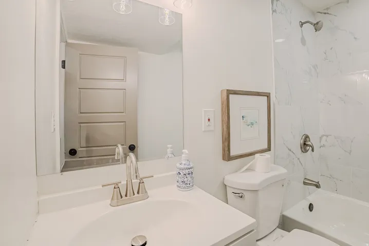Bathroom featuring a white vanity with a brushed nickel faucet, a large wall-mounted mirror, a tiled shower with a brushed nickel shower head, and a white toilet