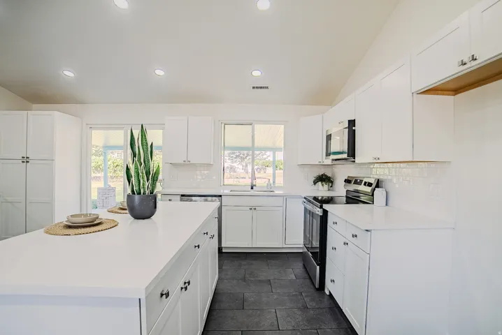 Spacious kitchen featuring an expansive center island with countertop seating, white shaker-style cabinetry, stainless steel appliances, and a subway tile backsplash