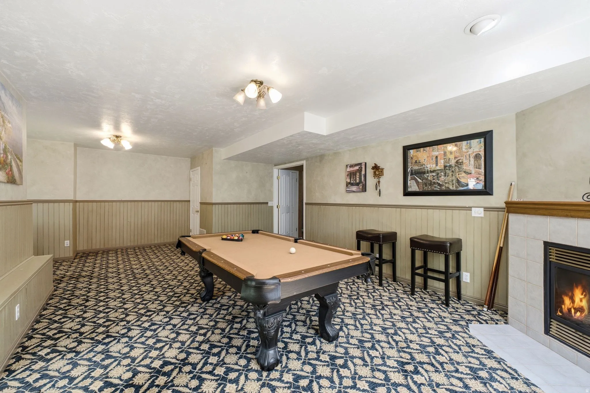 Recreation room featuring patterned carpet flooring, chair rail with wainscoting, and a fireplace with tile surround