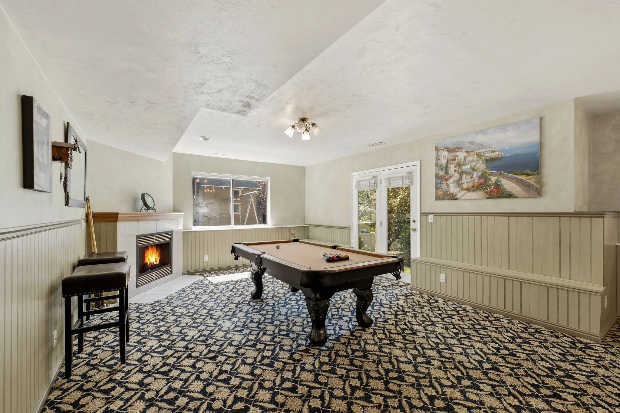 Spacious recreation room featuring a corner fireplace, beadboard wainscoting, and patterned carpet flooring