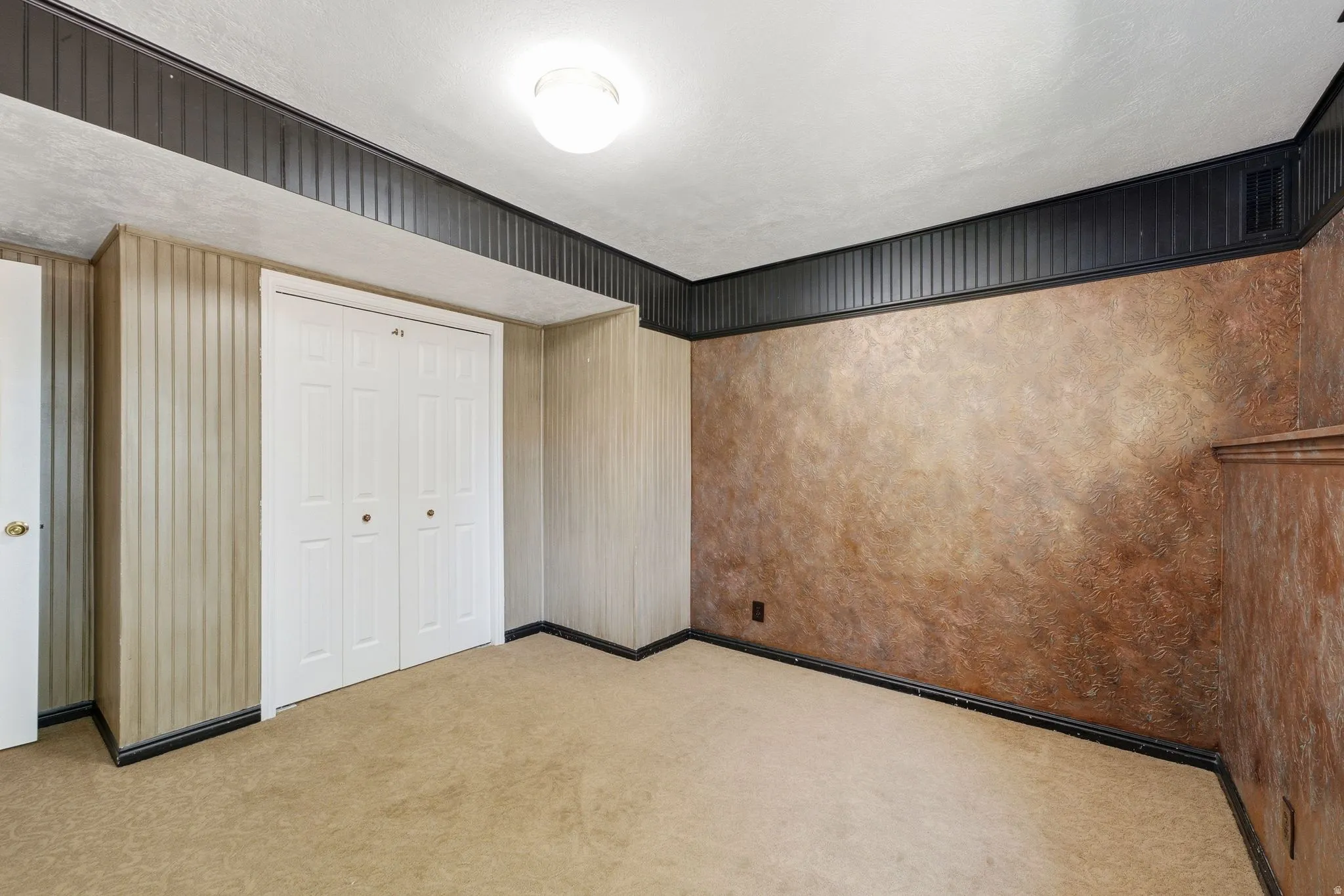 Carpeted room featuring a ceiling-mounted light fixture, white bi-fold closet doors, and a combination of vertical paneling and textured wall finishes