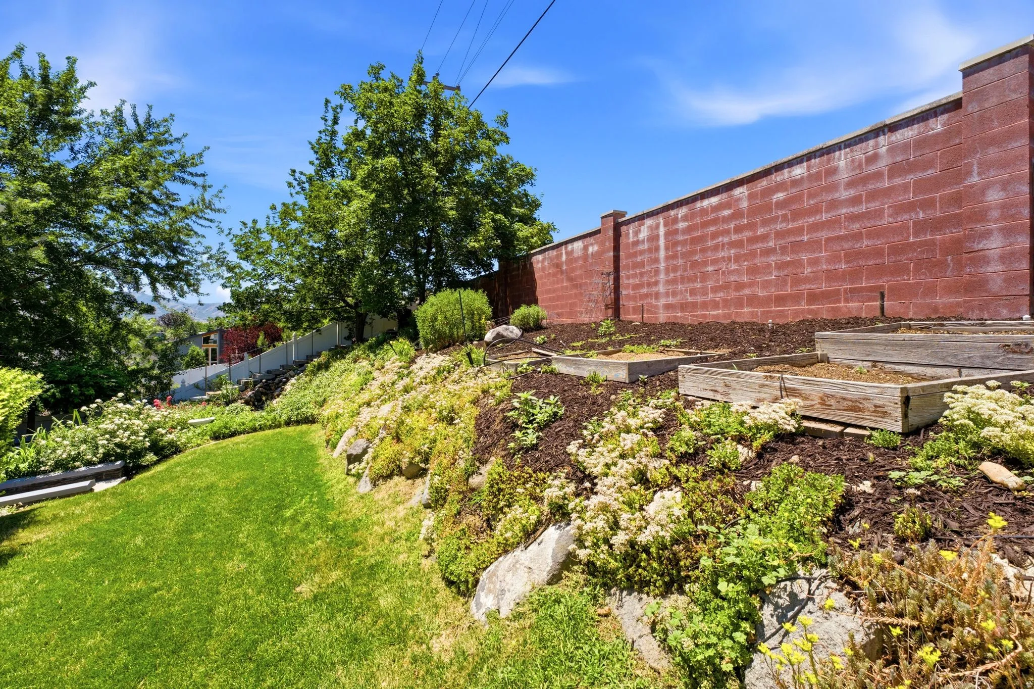 Terraced garden area featuring multiple planter boxes, a red brick privacy wall, and mature trees framing the property