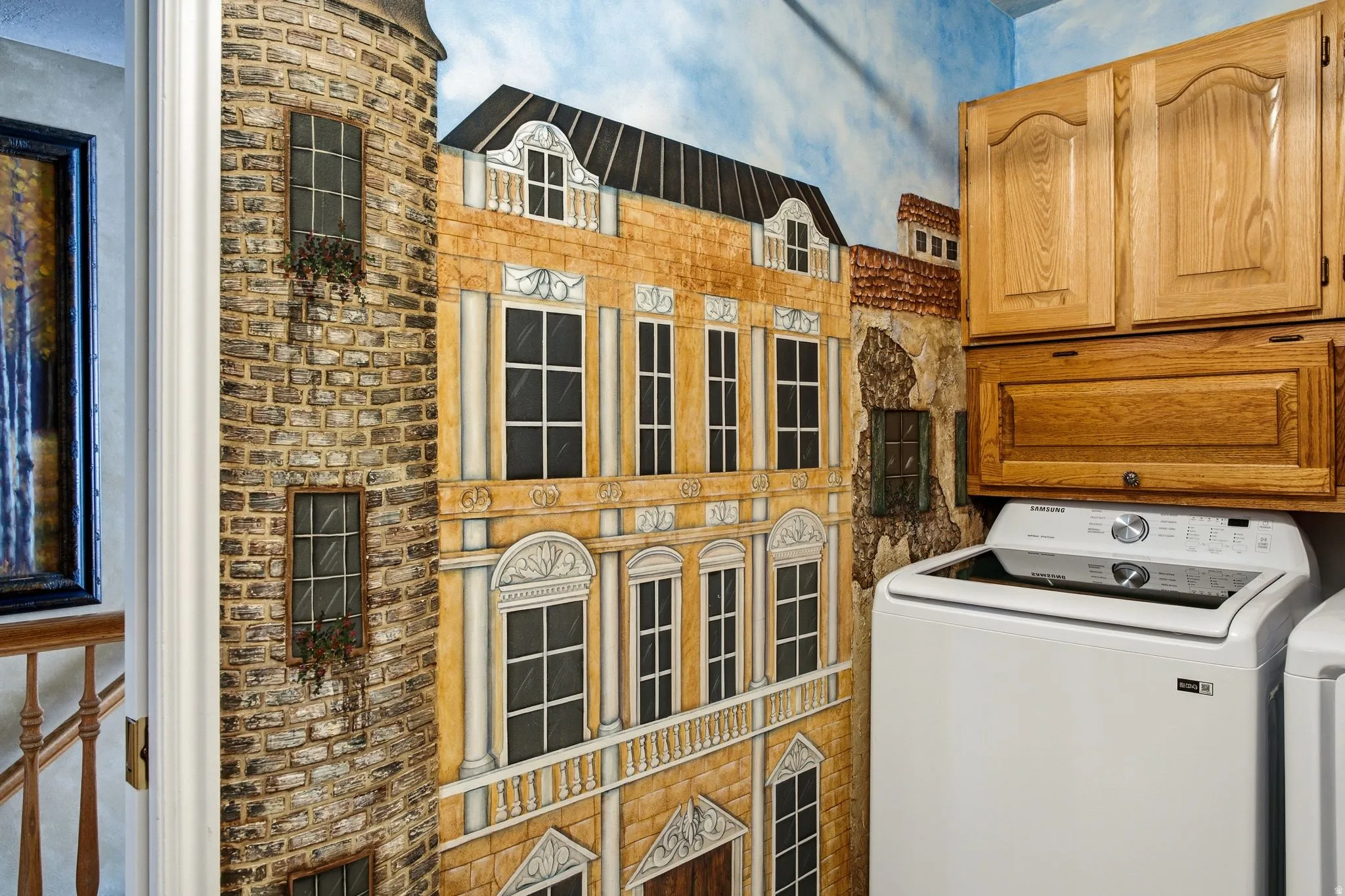 Laundry area featuring custom wall mural, built-in wooden cabinetry, and overhead storage