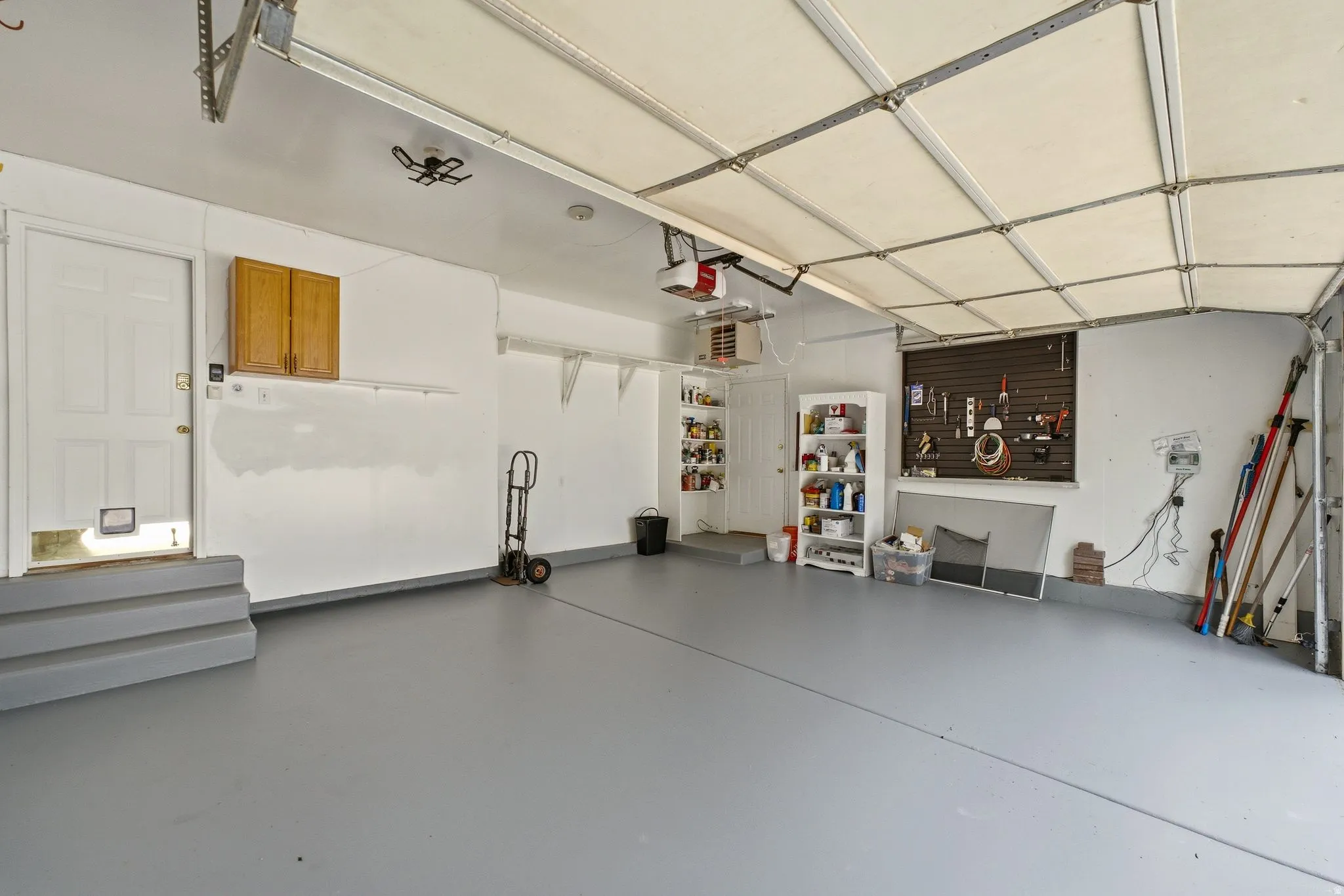 Spacious garage featuring a durable gray epoxy floor, overhead door, built-in shelving, and a wall-mounted pegboard system for organization