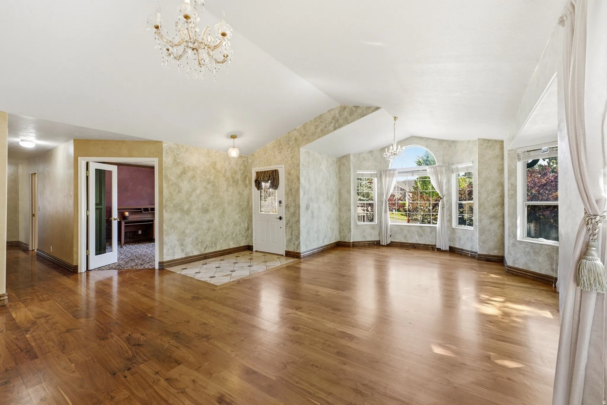 Spacious living area featuring high vaulted ceilings, wood-finish flooring, a decorative chandelier, and a bay window with multiple panes