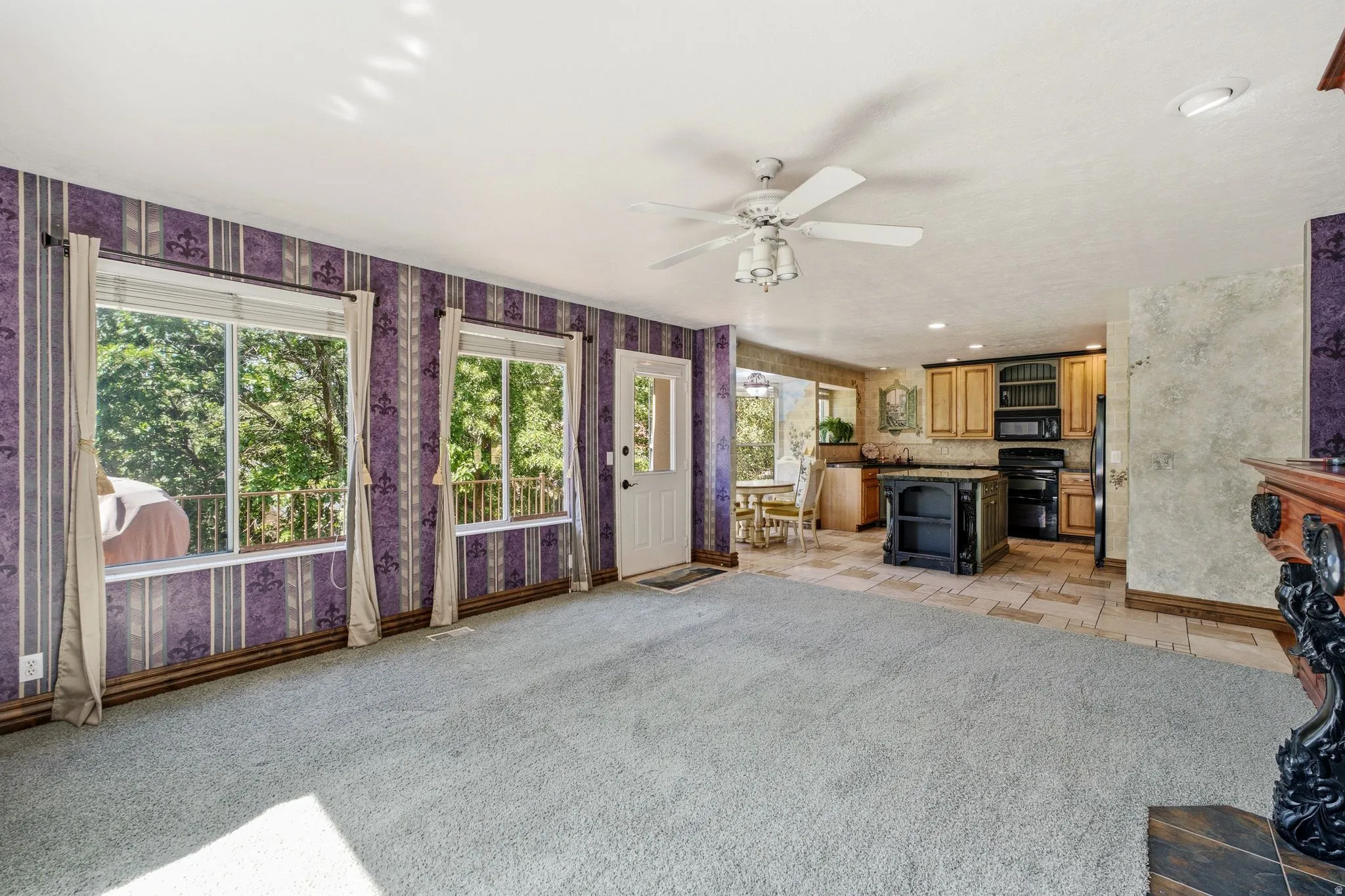 Open-concept living area featuring a ceiling fan, carpeted flooring, and multiple windows
