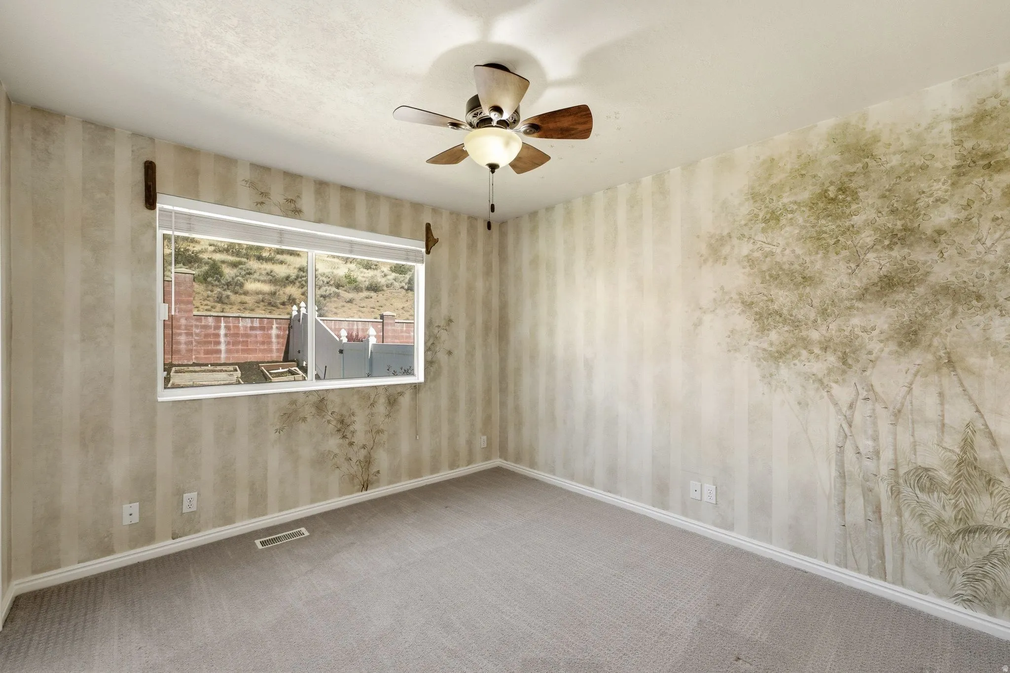 Room featuring wall-to-wall carpeting, a window overlooking a hillside, a ceiling fan with integrated lighting, and decorative wall treatments