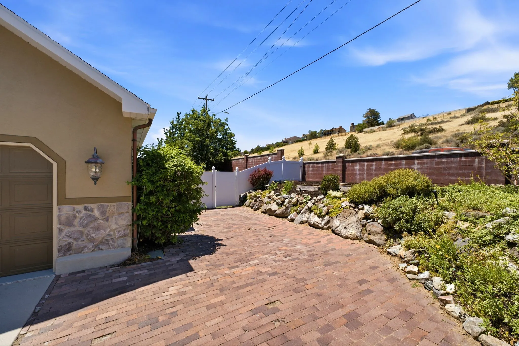 Brick paver driveway leading to a private side yard with a white privacy fence