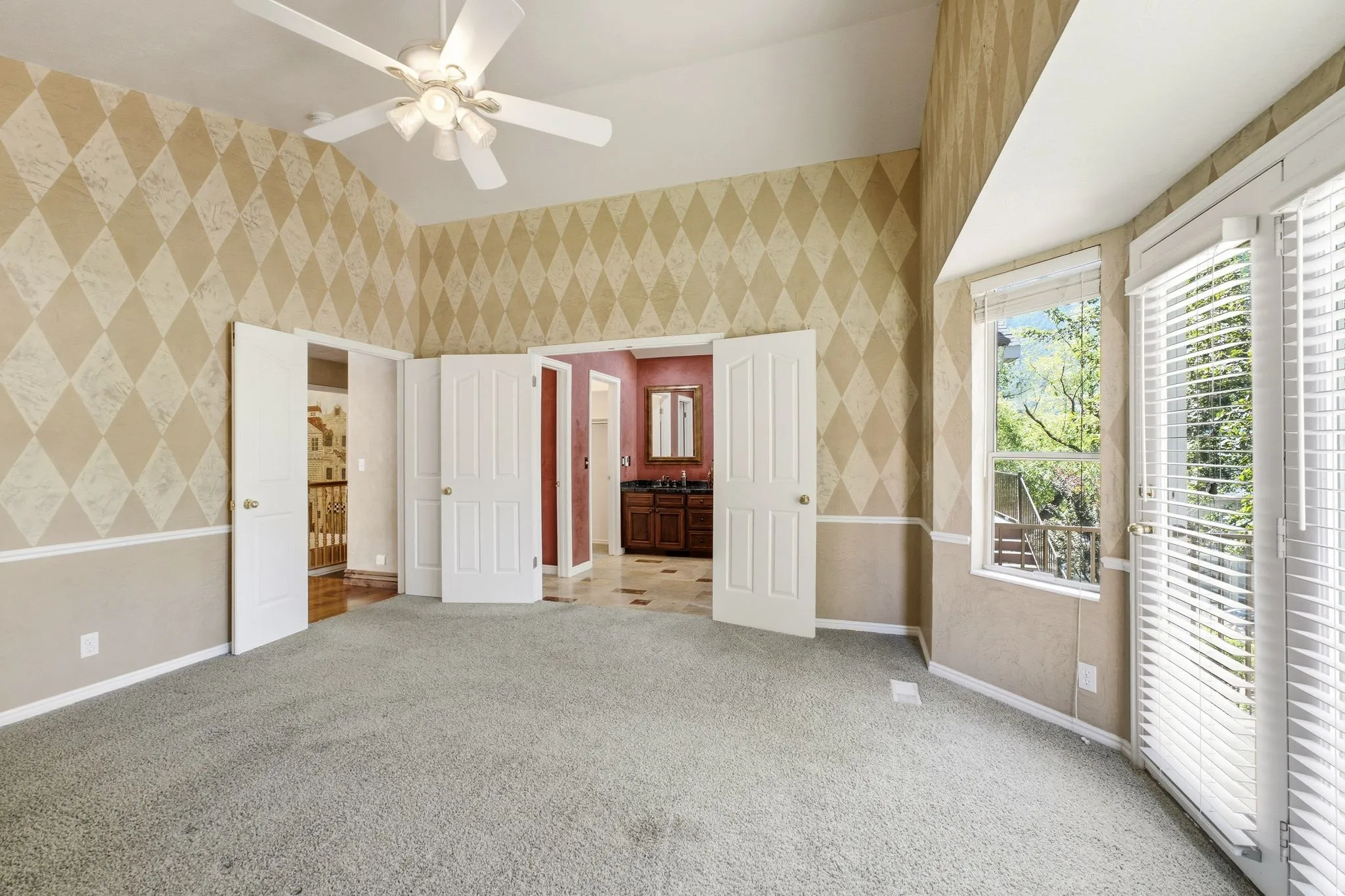 Vaulted ceiling room featuring patterned wallpaper, a ceiling fan, and a large window with white blinds