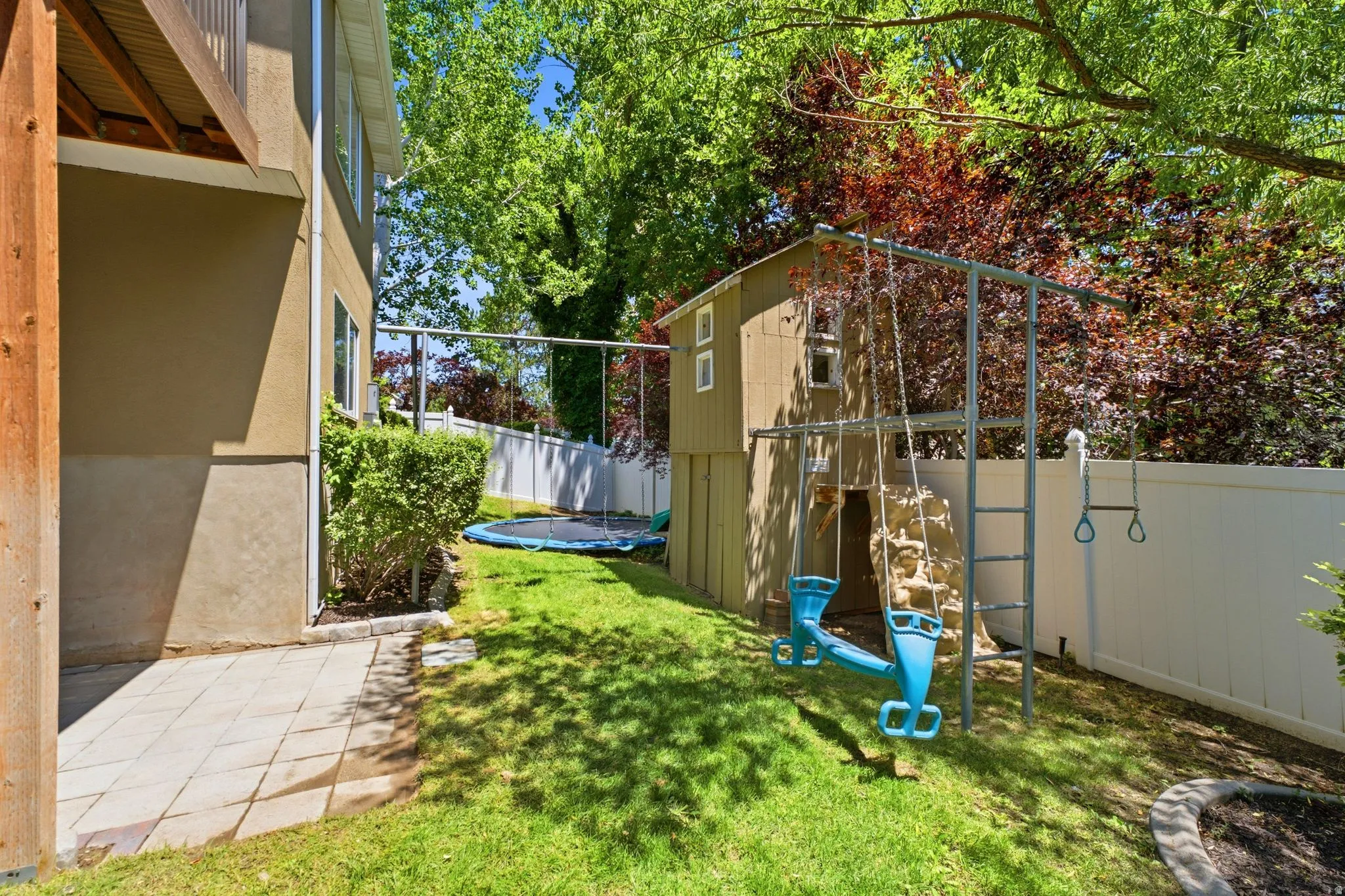 Expansive backyard with a manicured lawn, paved patio area, and mature trees providing shade