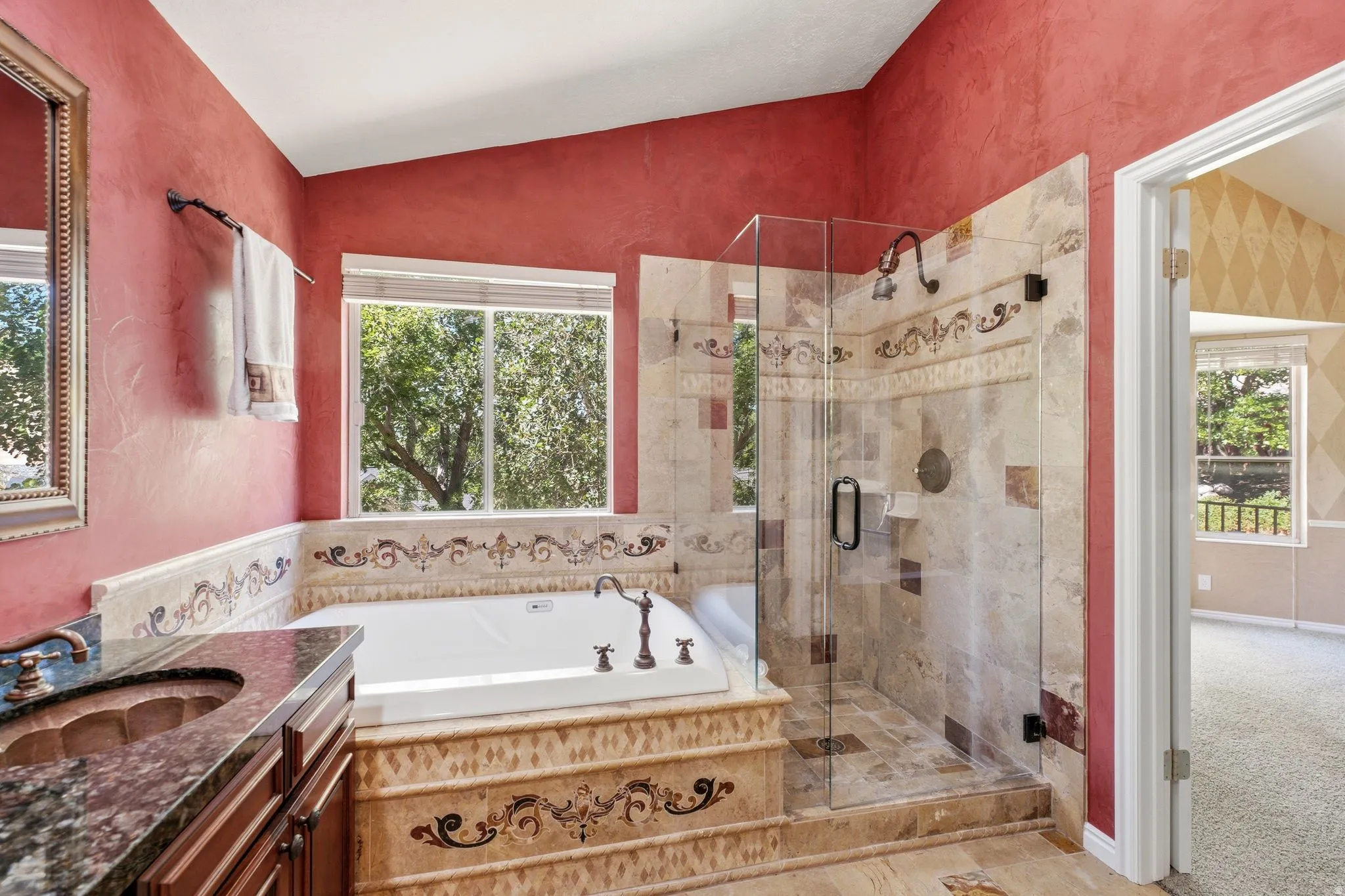Bathroom featuring a built-in soaking tub, a separate glass-enclosed shower, a vanity with an undermount sink and stone countertop, tile flooring, and a window providing natural light