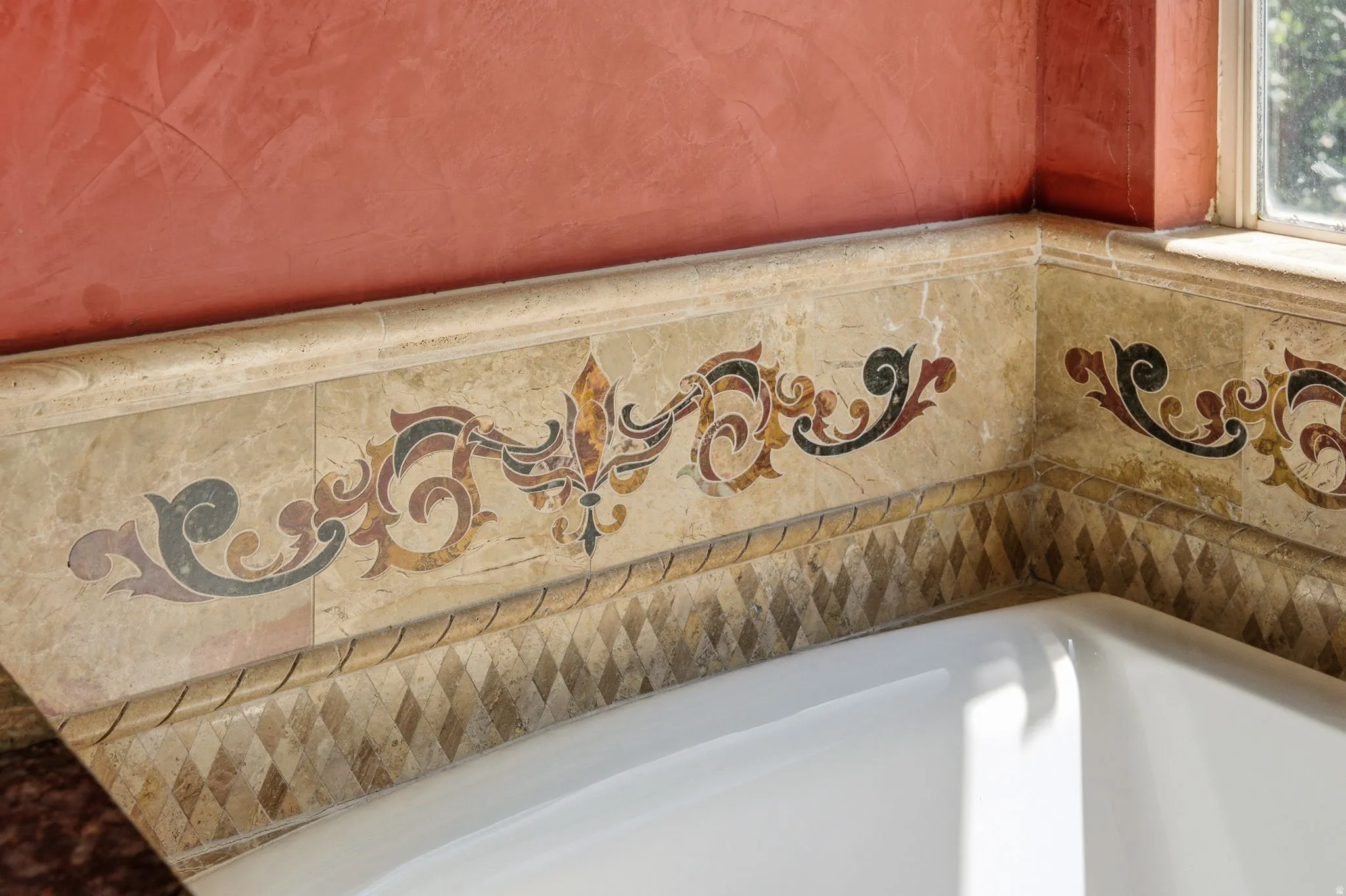 Bathtub surround featuring ornate tile work, a decorative mosaic border, and a textured wall finish