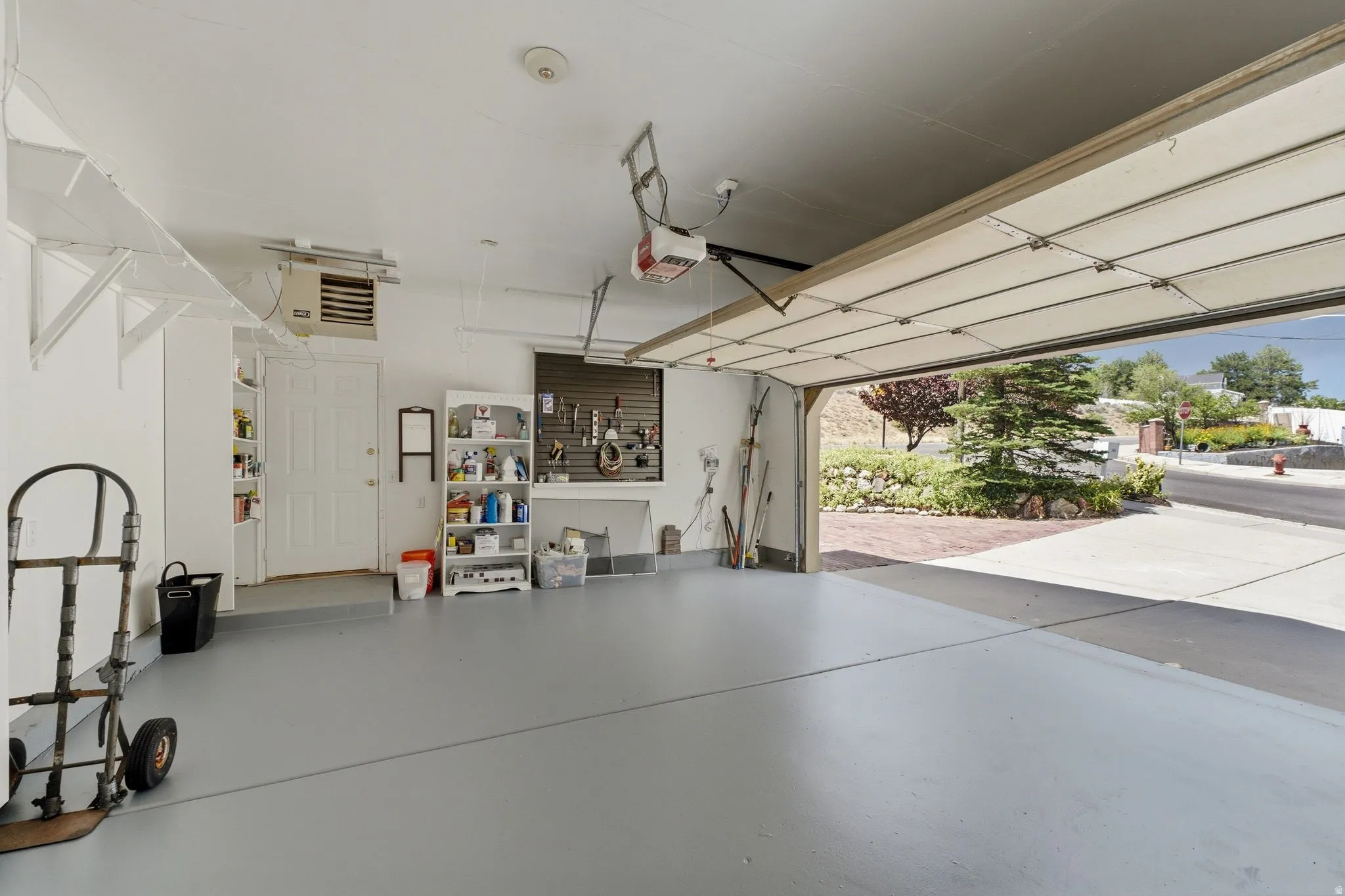 Spacious garage featuring a light gray floor finish, built-in shelving, a wall-mounted heater, and a white paneled door