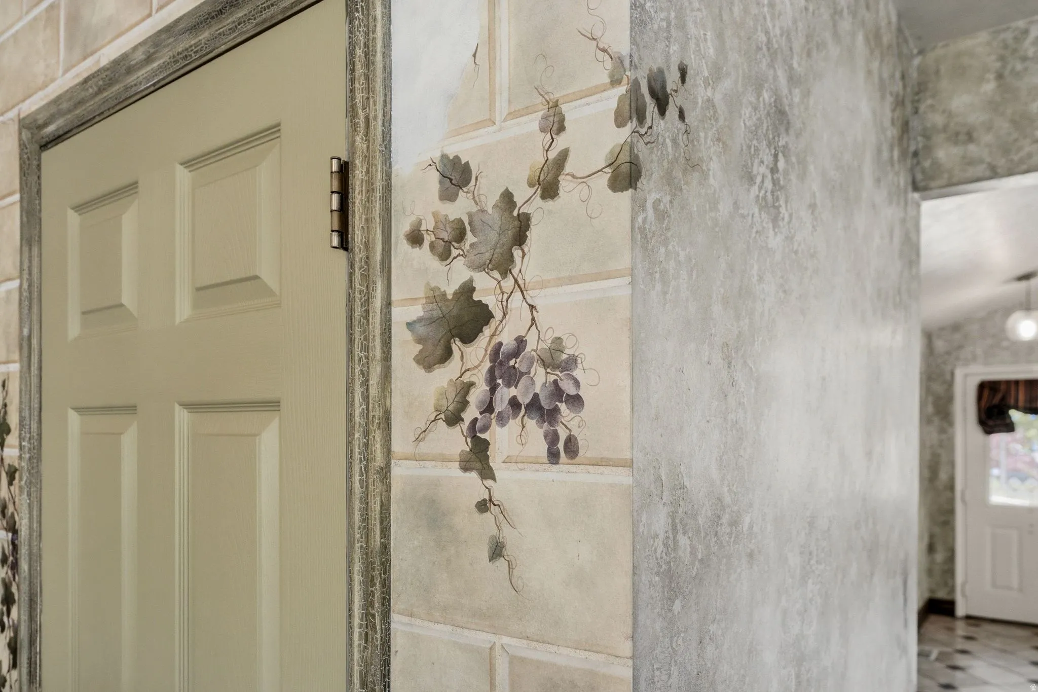 Six-panel interior door with distressed trim, complemented by a wall mural featuring grapevines and a textured wall finish