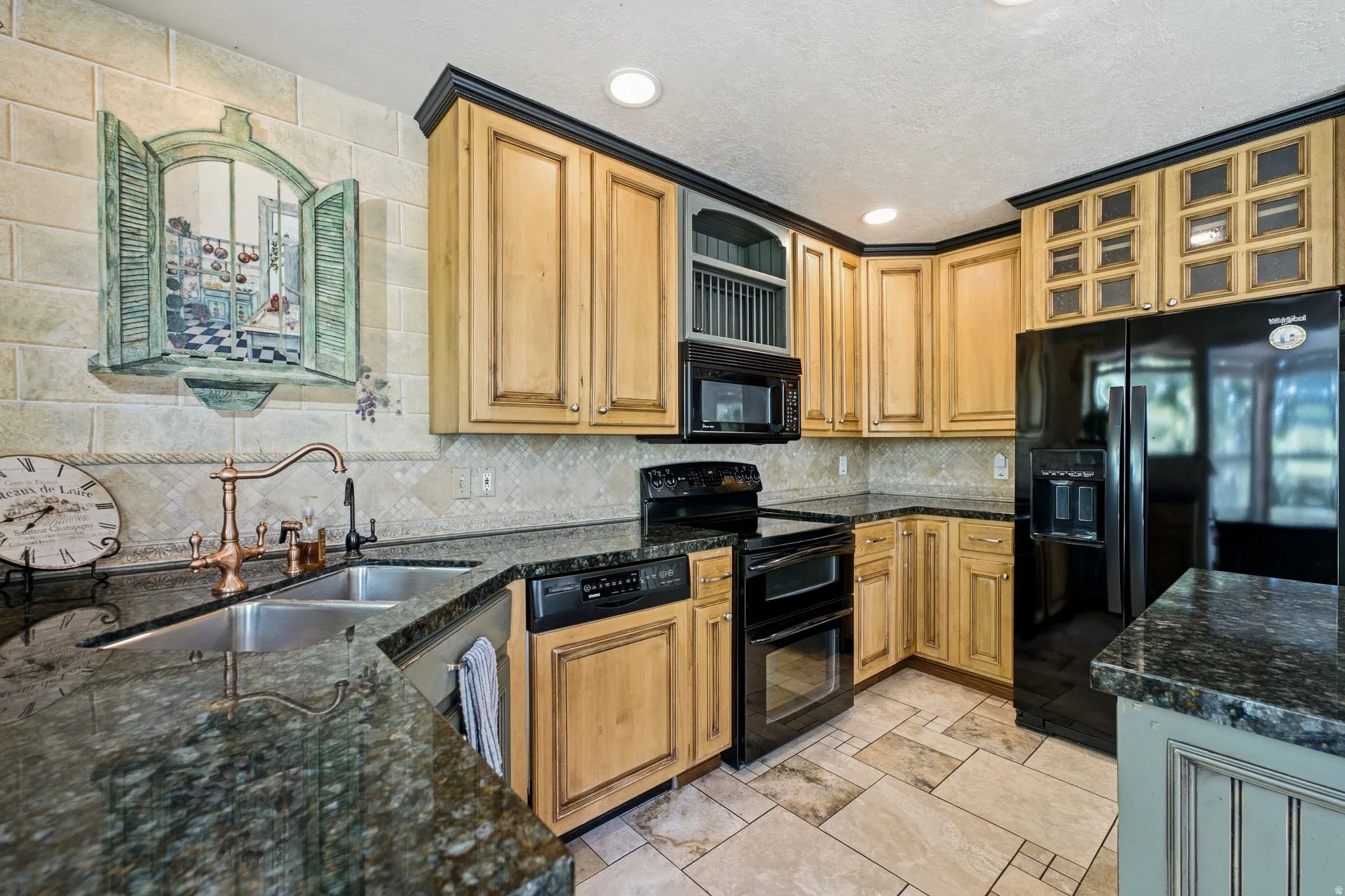 Kitchen featuring light wood cabinetry with dark trim, black appliances, stone-finish countertops, and a tile backsplash
