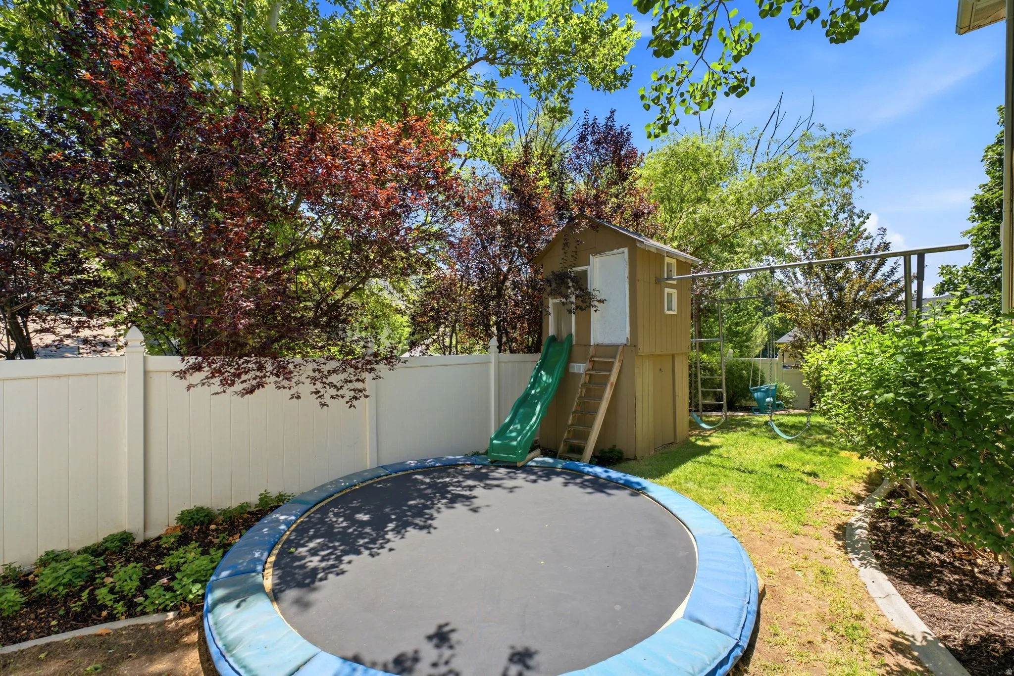 Fenced backyard featuring mature trees, a playhouse with a slide, and a swing set
