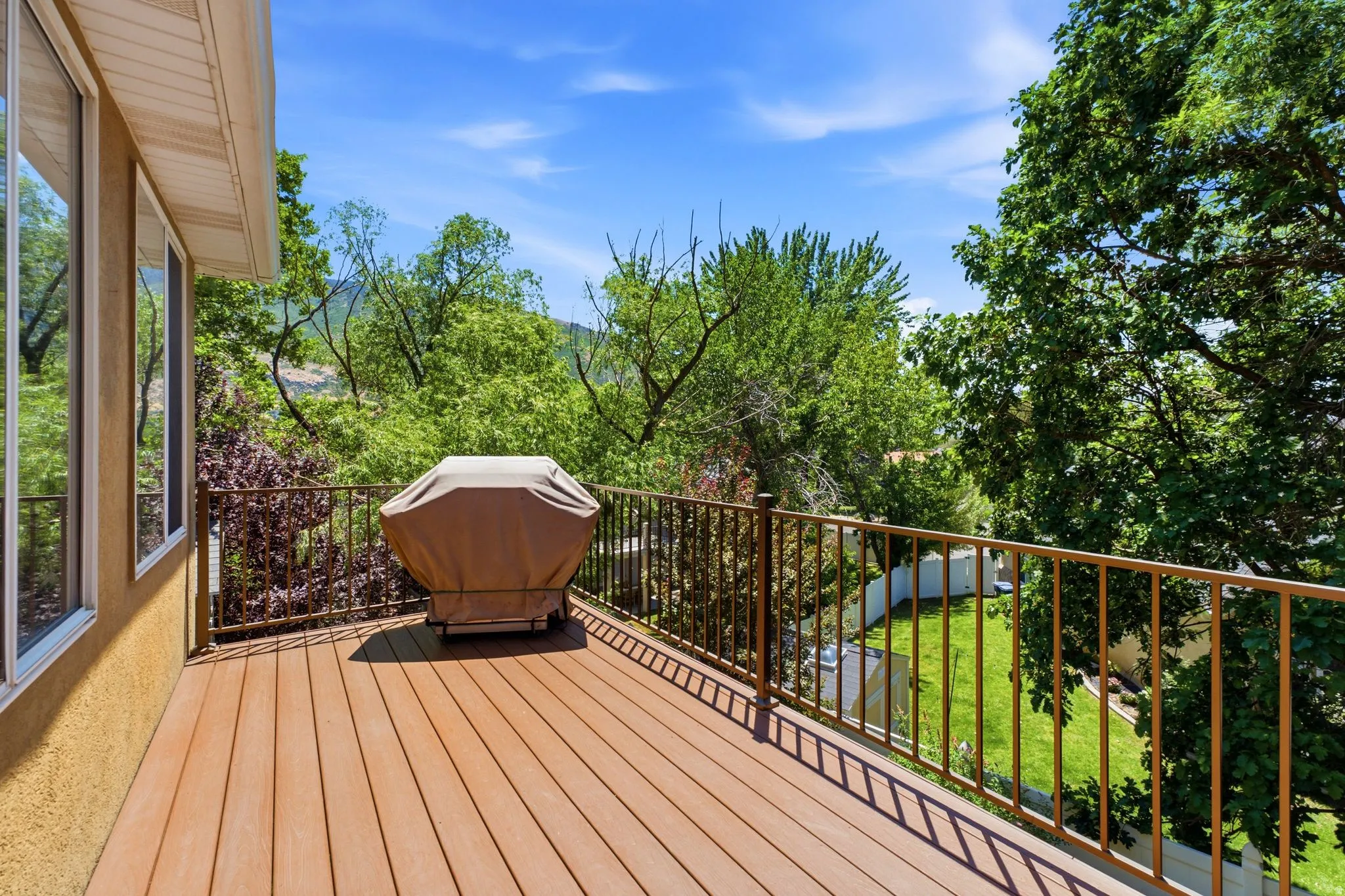 Expansive wood-finish deck featuring a brown metal railing, stucco exterior, and multiple large windows