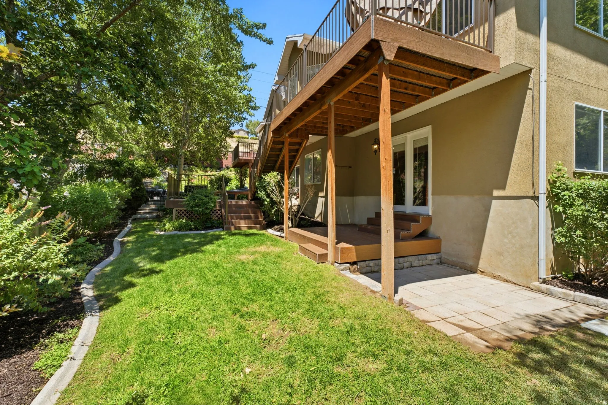 Expansive backyard featuring a manicured lawn, established landscaping, and a multi-level wooden deck