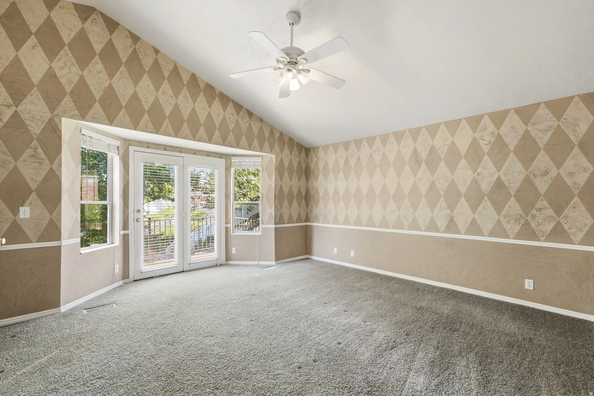 Vaulted ceiling room featuring patterned walls, light-toned carpeting, and a ceiling fan
