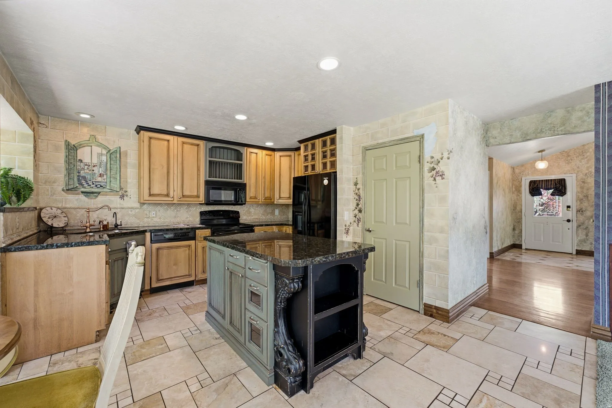 Kitchen featuring an island with carved details, dark countertops, black appliances, light wood-finish cabinetry, and tiled flooring