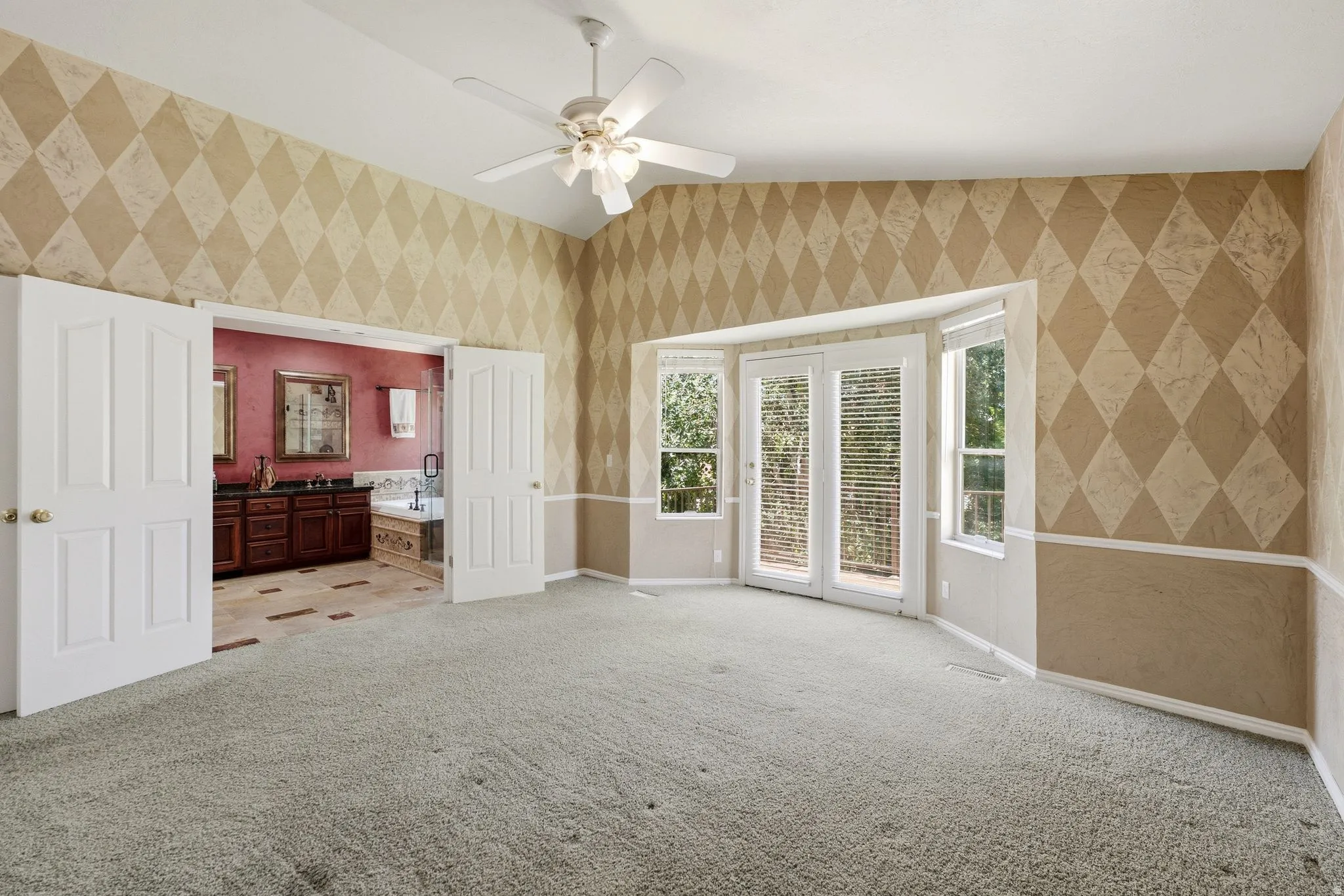 Spacious room featuring carpeting, a vaulted ceiling with a ceiling fan, and a bay window with French doors