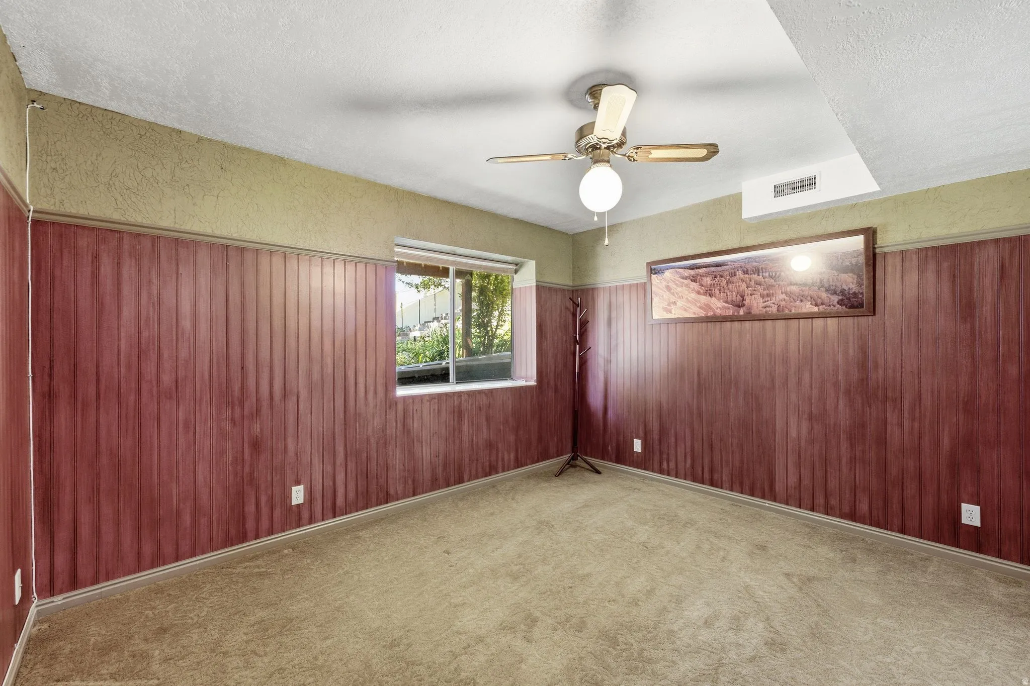Carpeted room featuring a window with exterior foliage, horizontal wood paneling, and a ceiling fan with light fixture