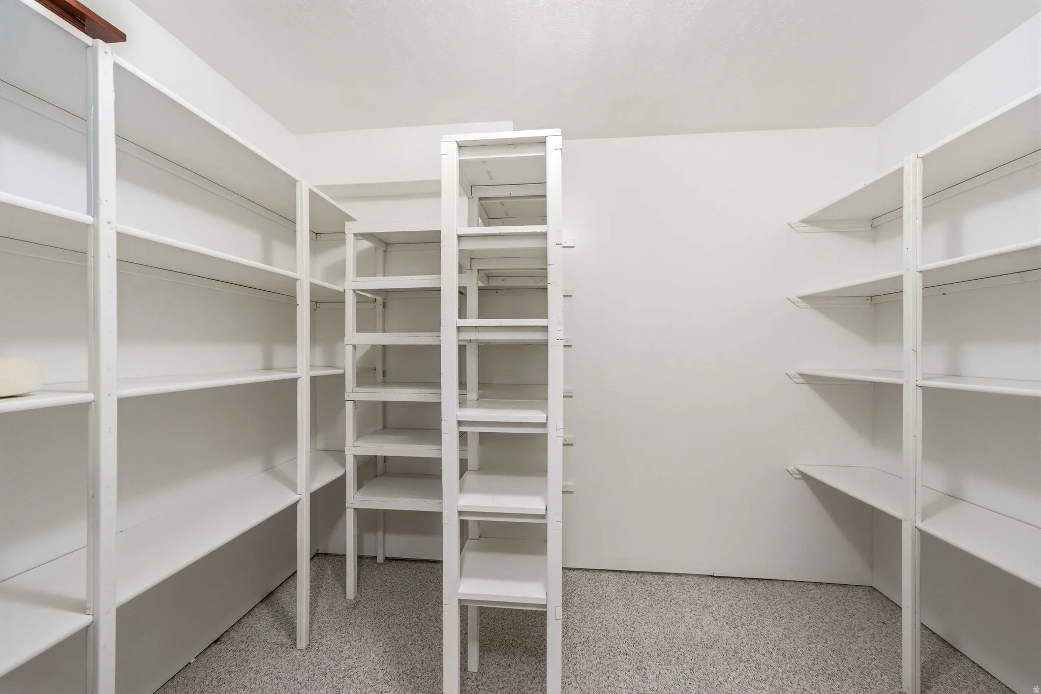 Walk-in closet featuring extensive built-in shelving, white painted walls, and textured flooring