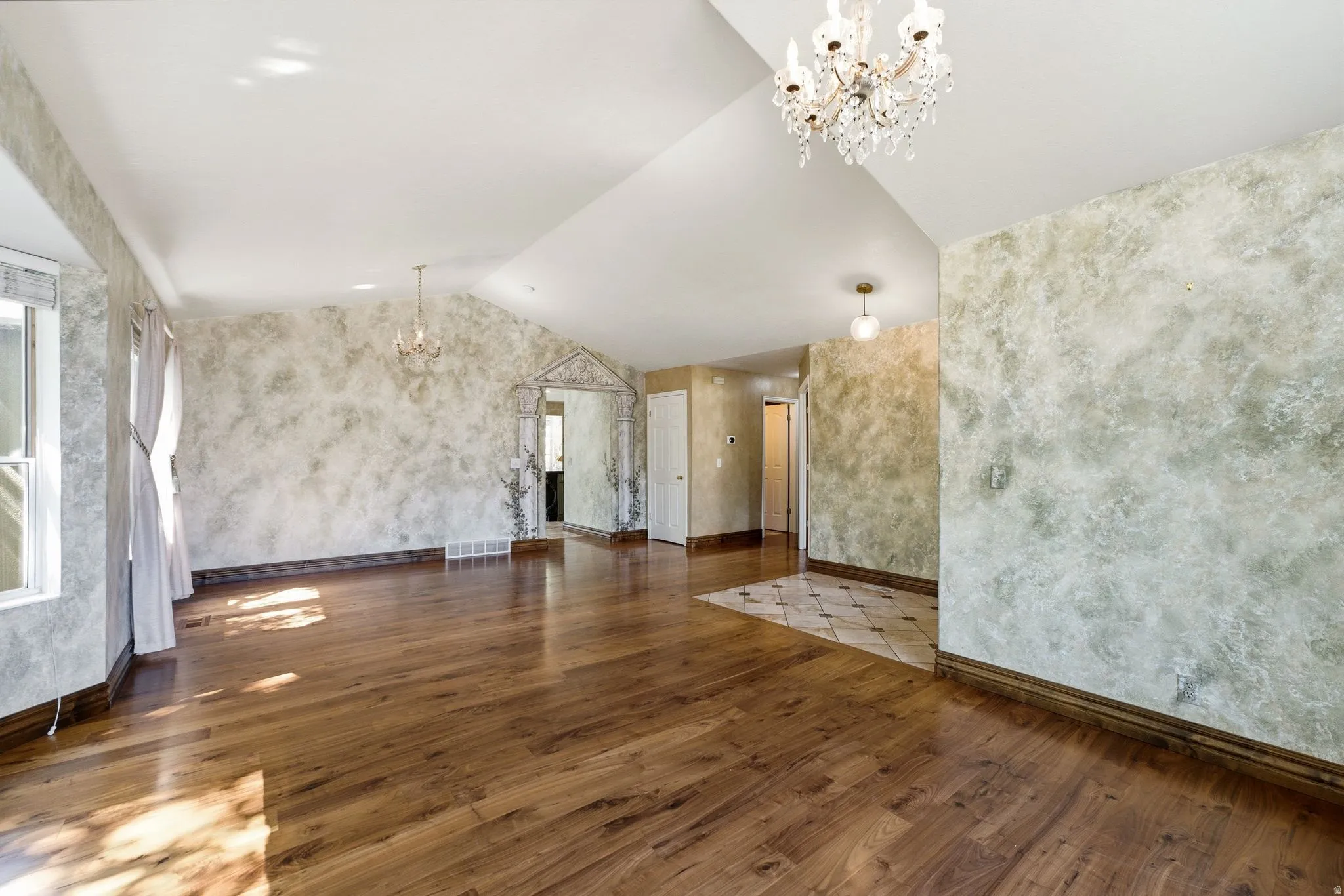 Spacious interior room featuring wood-finish flooring, vaulted ceilings, and textured wall finishes