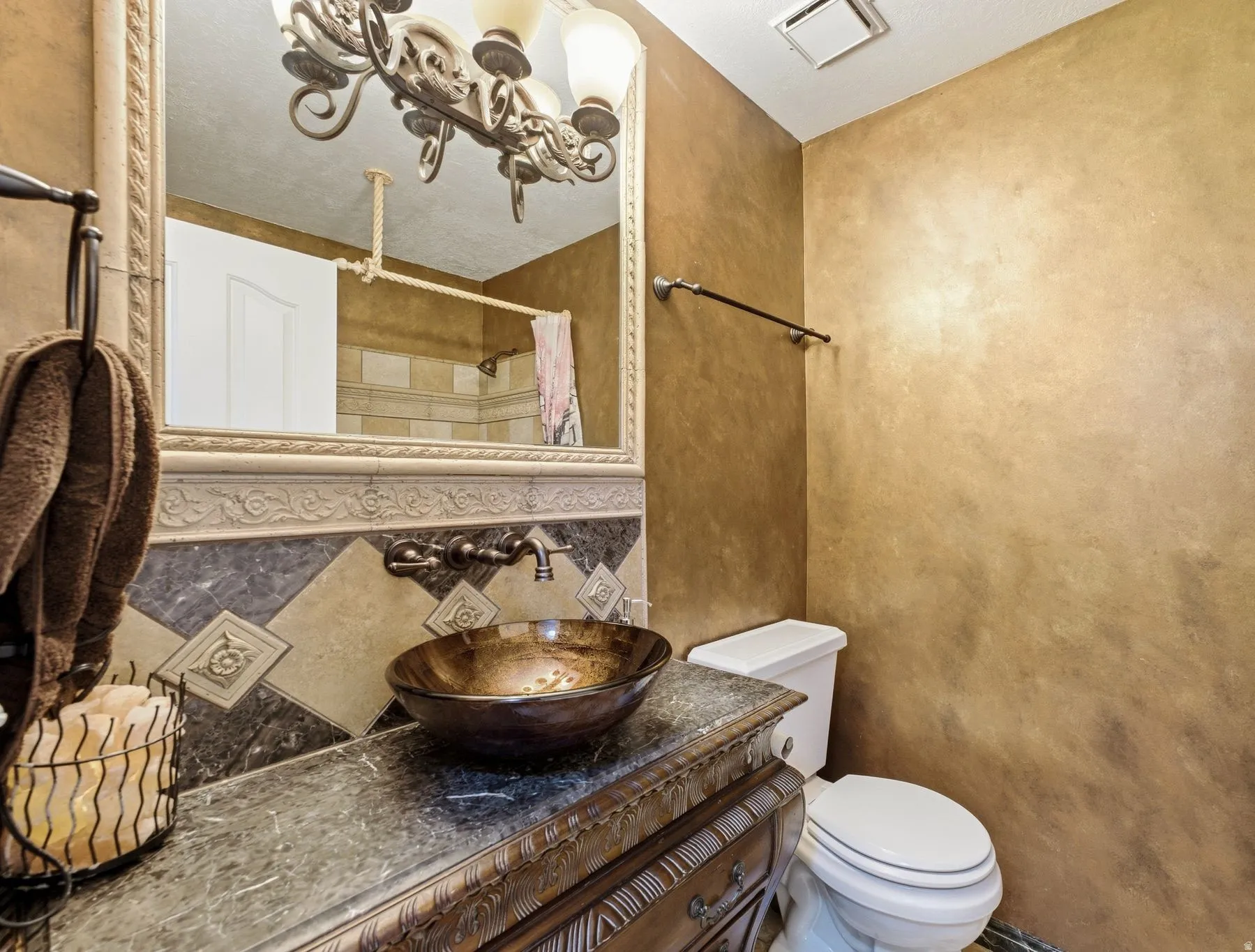 Vanity featuring a vessel sink with wall-mounted bronze-finish faucet, dark stone countertop, and carved wood-finish cabinetry