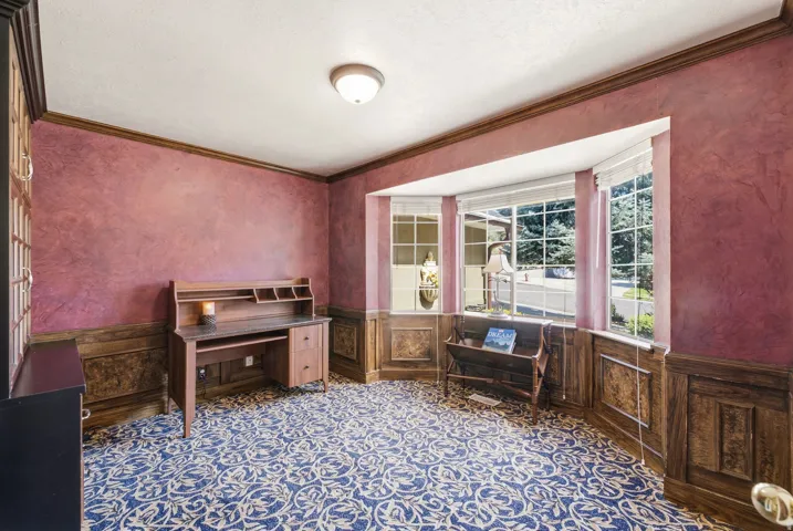 Bay window with multiple panes, wood-paneled wainscoting, and patterned carpet flooring