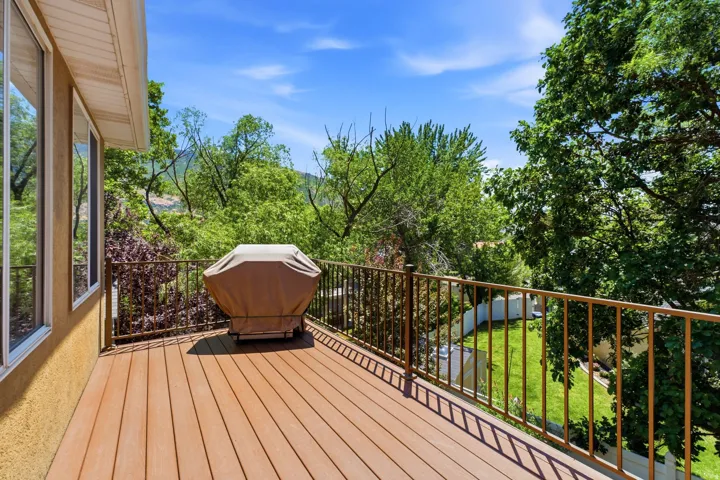 Expansive wood-finish deck featuring a brown metal railing, stucco exterior, and multiple large windows