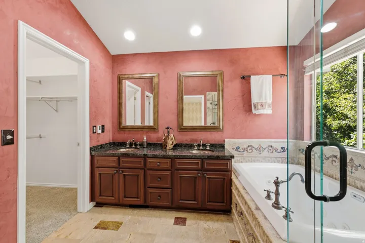 Bathroom featuring a dual vanity with a dark granite countertop, a built-in jetted tub, a glass-enclosed shower, and tile flooring