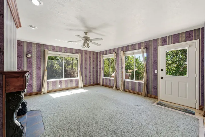 Living area featuring multiple windows, a ceiling fan, patterned wallpaper, and a fireplace with a dark wood mantel