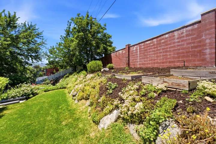 Terraced garden area featuring multiple planter boxes, a red brick privacy wall, and mature trees framing the property