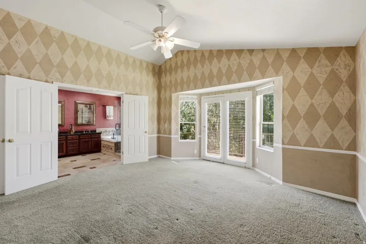 Spacious room featuring carpeting, a vaulted ceiling with a ceiling fan, and a bay window with French doors