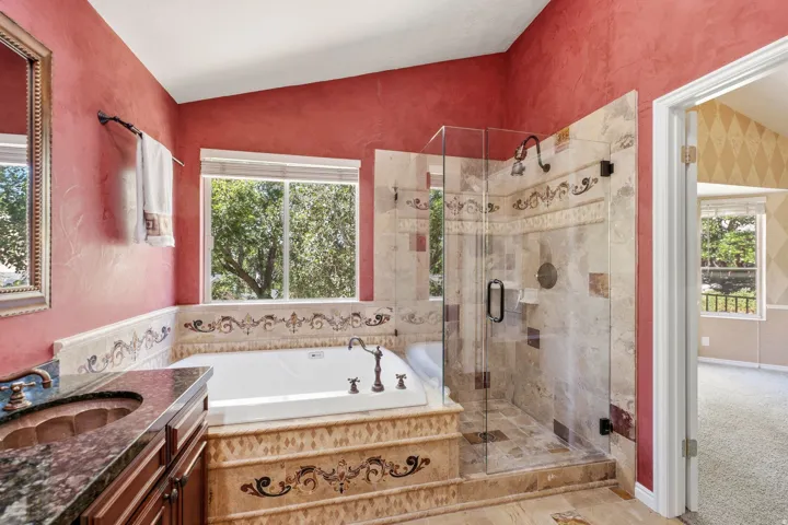 Bathroom featuring a built-in soaking tub, a separate glass-enclosed shower, a vanity with an undermount sink and stone countertop, tile flooring, and a window providing natural light
