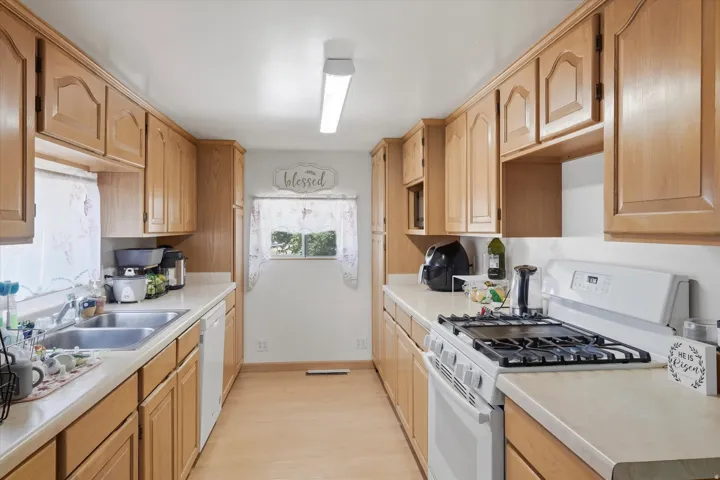 Galley kitchen featuring wood-finish cabinetry, light-toned countertops, and a double basin stainless steel sink