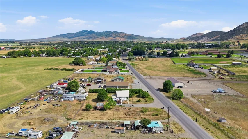 Expansive aerial view showcasing a rural landscape with agricultural fields, scattered residential structures, and distant mountains under a blue sky